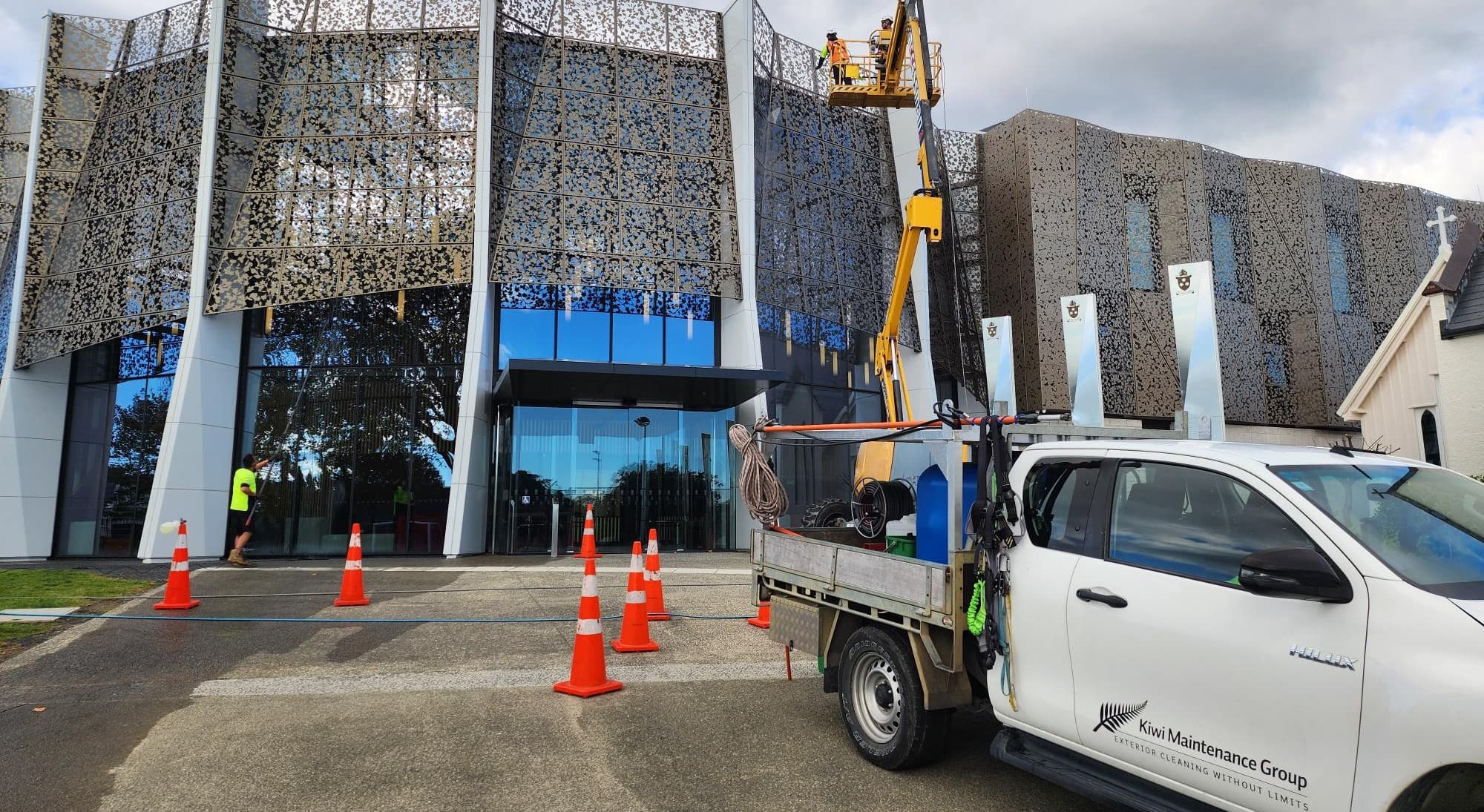 Kiwi Maintenance Group crew and branded ute on site at a commercial building, operator working at height in a boom lift
